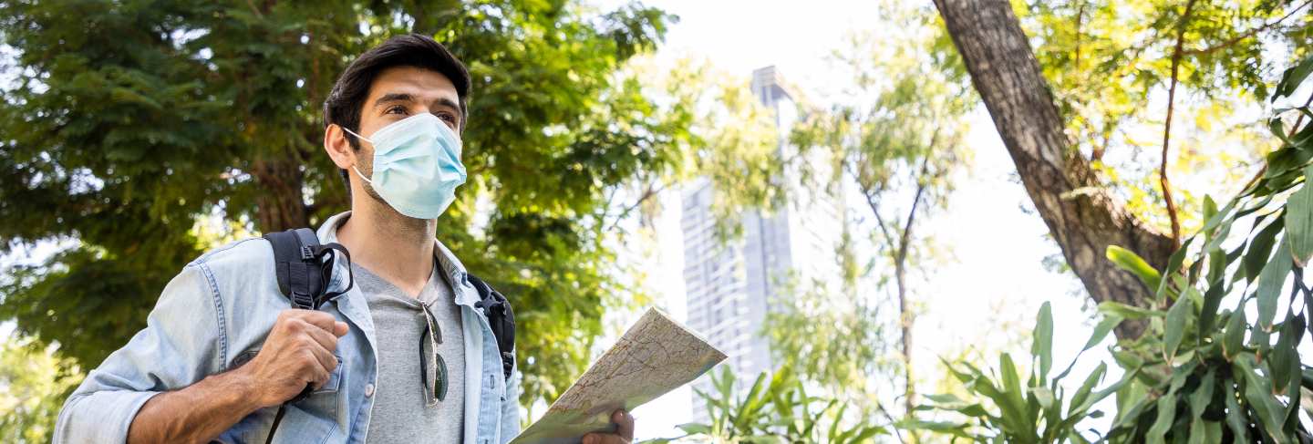 Young handsome man looking paper map and using sun glasses in public park with a happy face standing and smiling