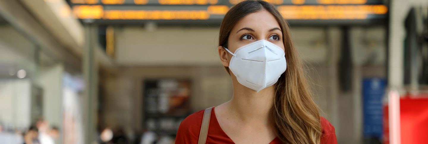 Traveler woman wearing kn95 ffp2 face mask at train station to protect from virus and smog.