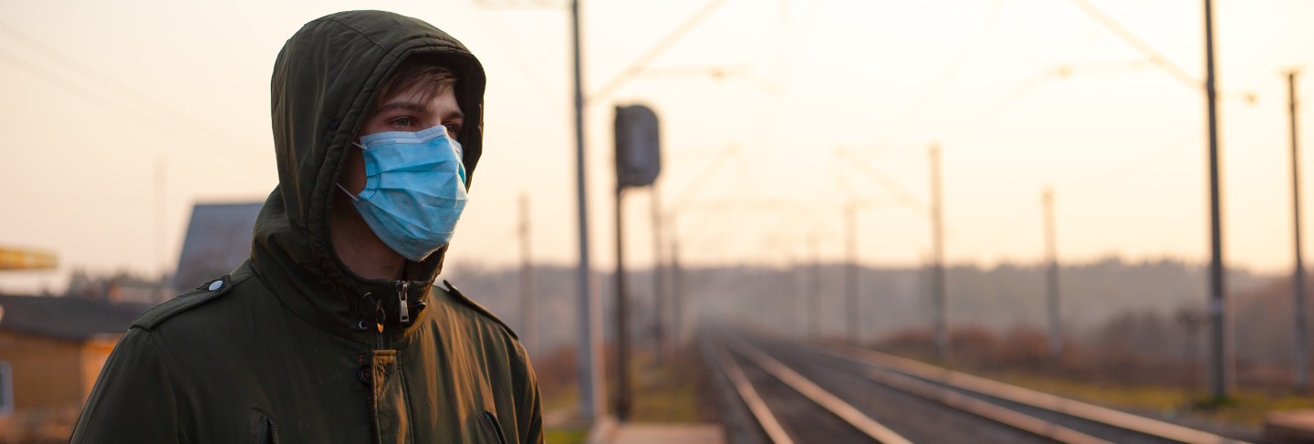 Guy in disposable medical mask standing at train station on sunset.