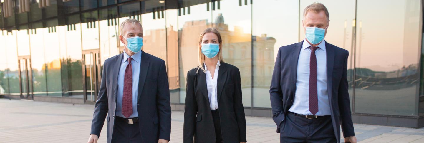 Business tourists in face masks visiting foreign partner office, wheeling suitcase, walking outdoors. front view. business trip and epidemic concept