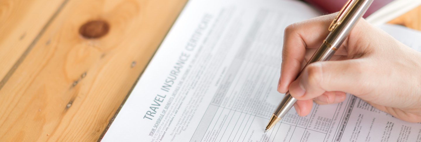 Hand with pen over travel aviation insurance application form and passport