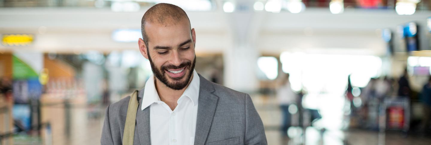 Smiling businessman holding a boarding pass and checking his mobile phone
