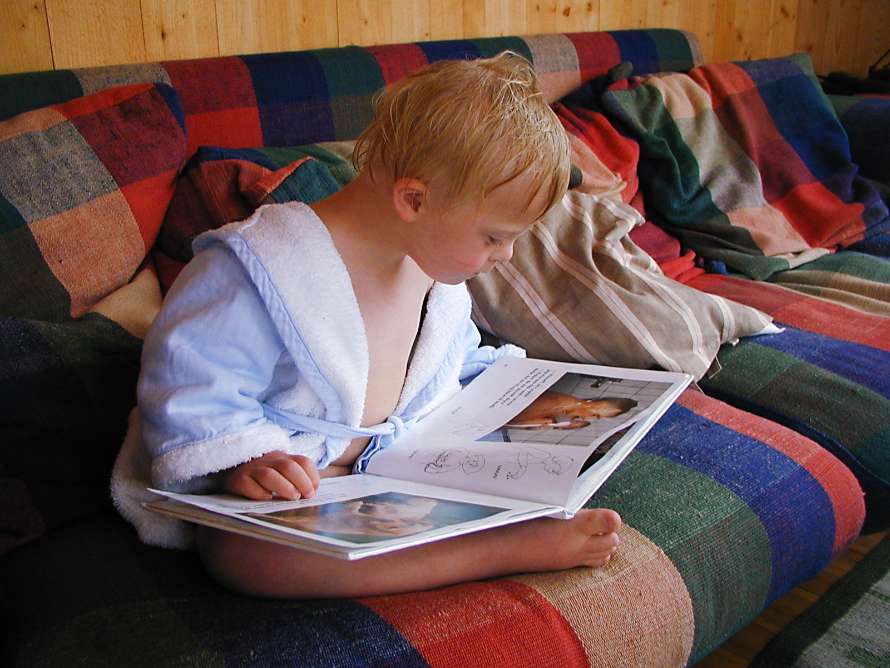 Barnet läser en bok i soffan.