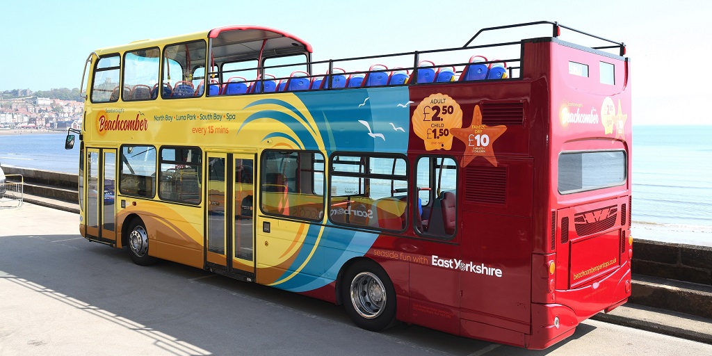 A colourful open top bus with Scarborough's South Bay in the background