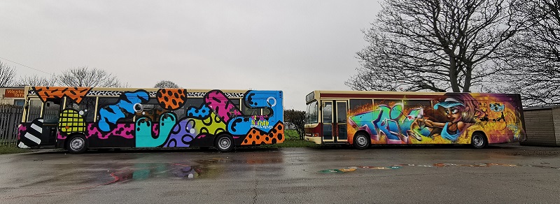 Two single deck buses with graffiti parked in school car park