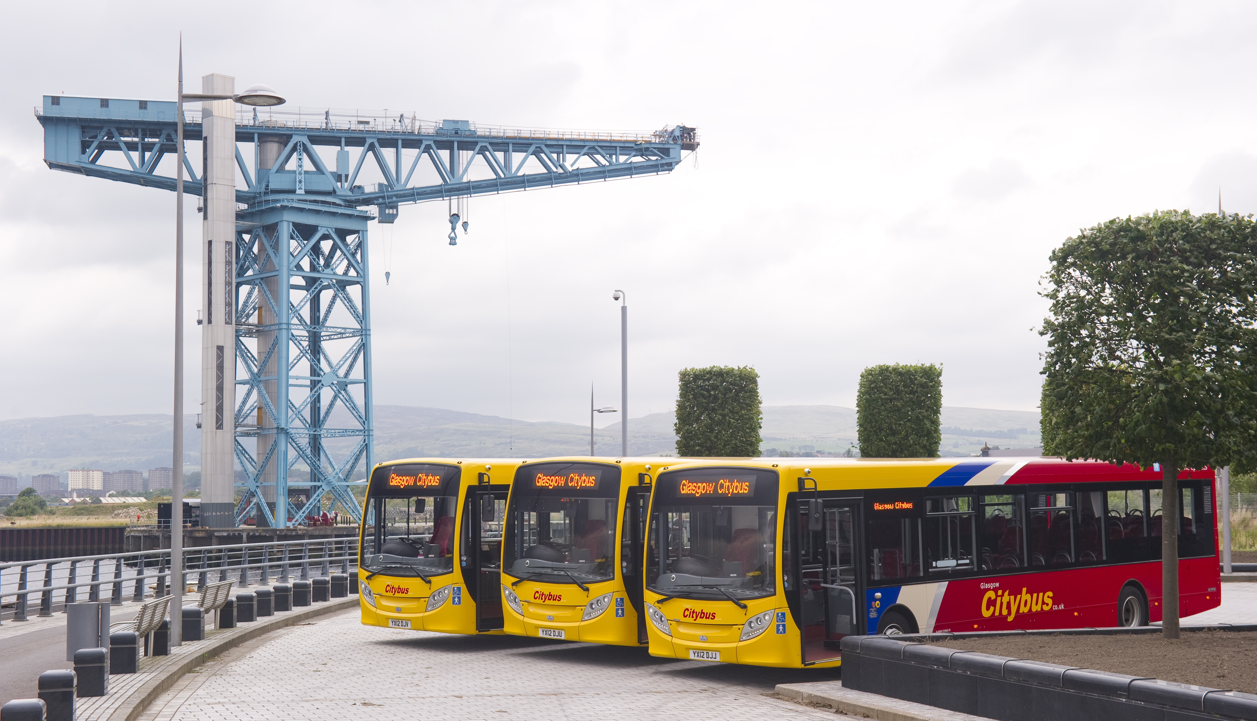 three yellow and red buses in front of the blue titan crane