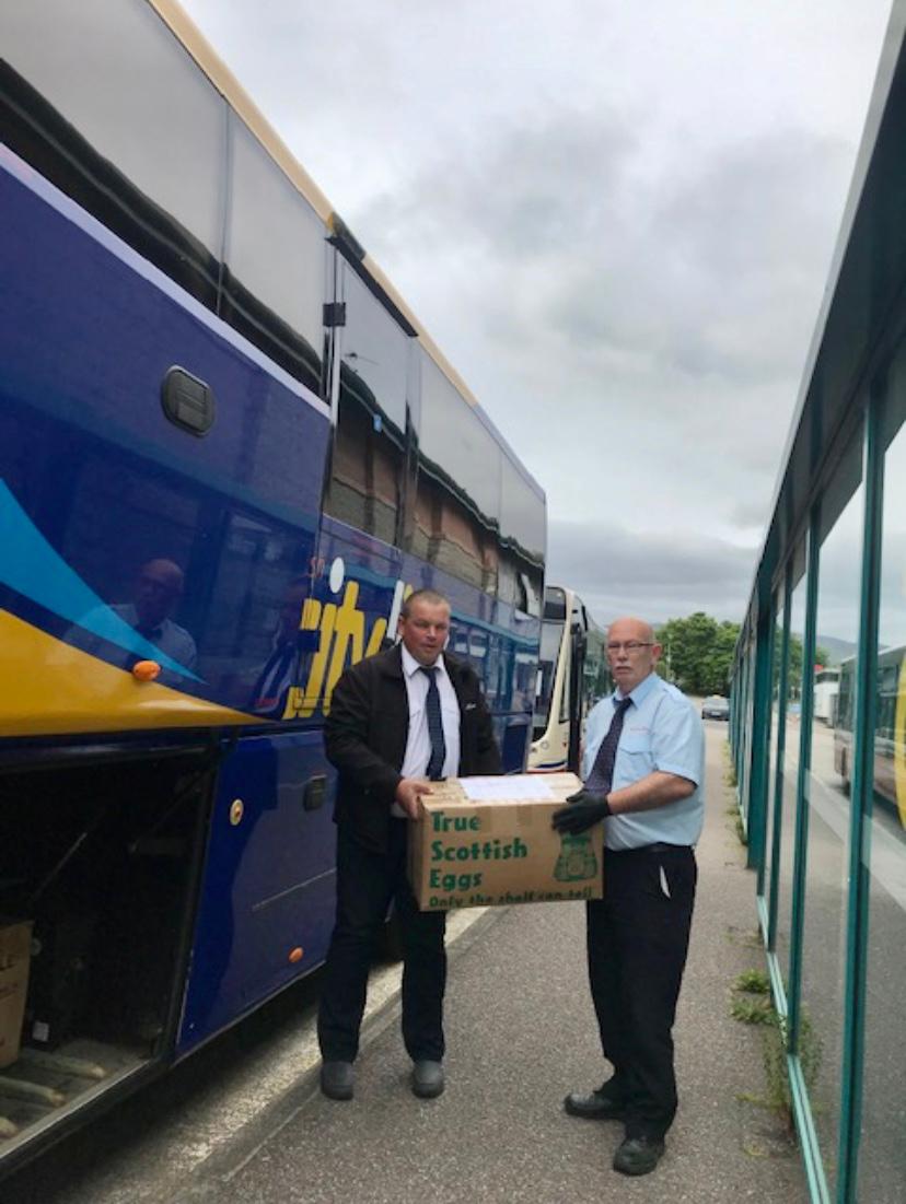 two men standing in front of blue coach holding boxes