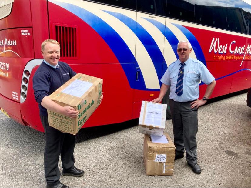 two men standing in front of red coach holding boxes
