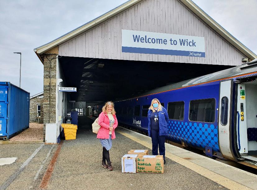 two women stand with cardboard boxes in front of Wick train station
