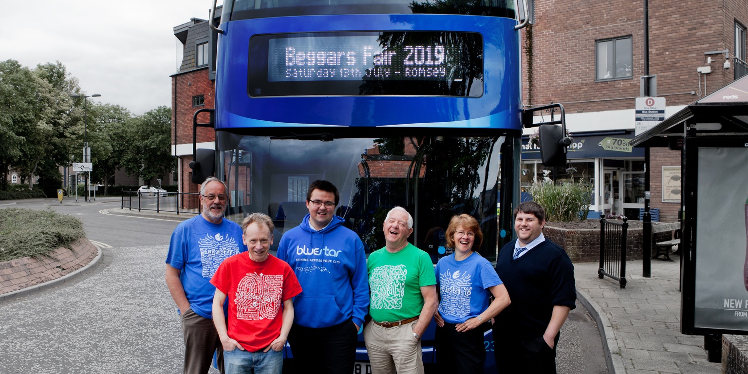 Representatives from the Beggars Fair and Bluestar pose laughing in front of a bus
