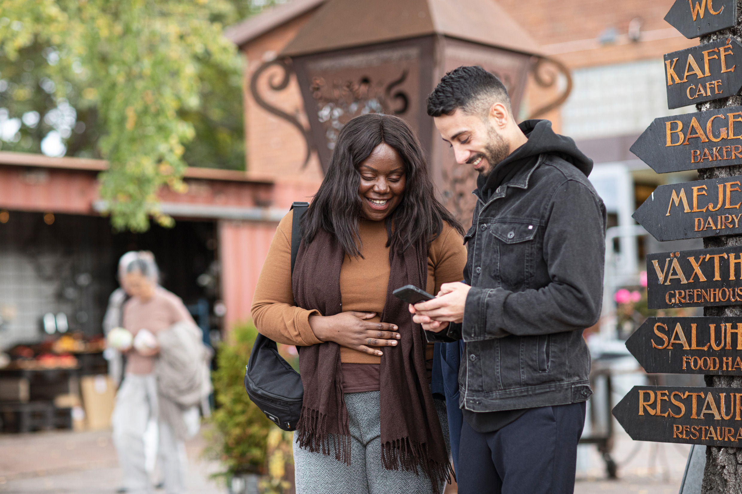 Två personer står utanför ett besöksmål och tittar gemensamt på en telefon.
