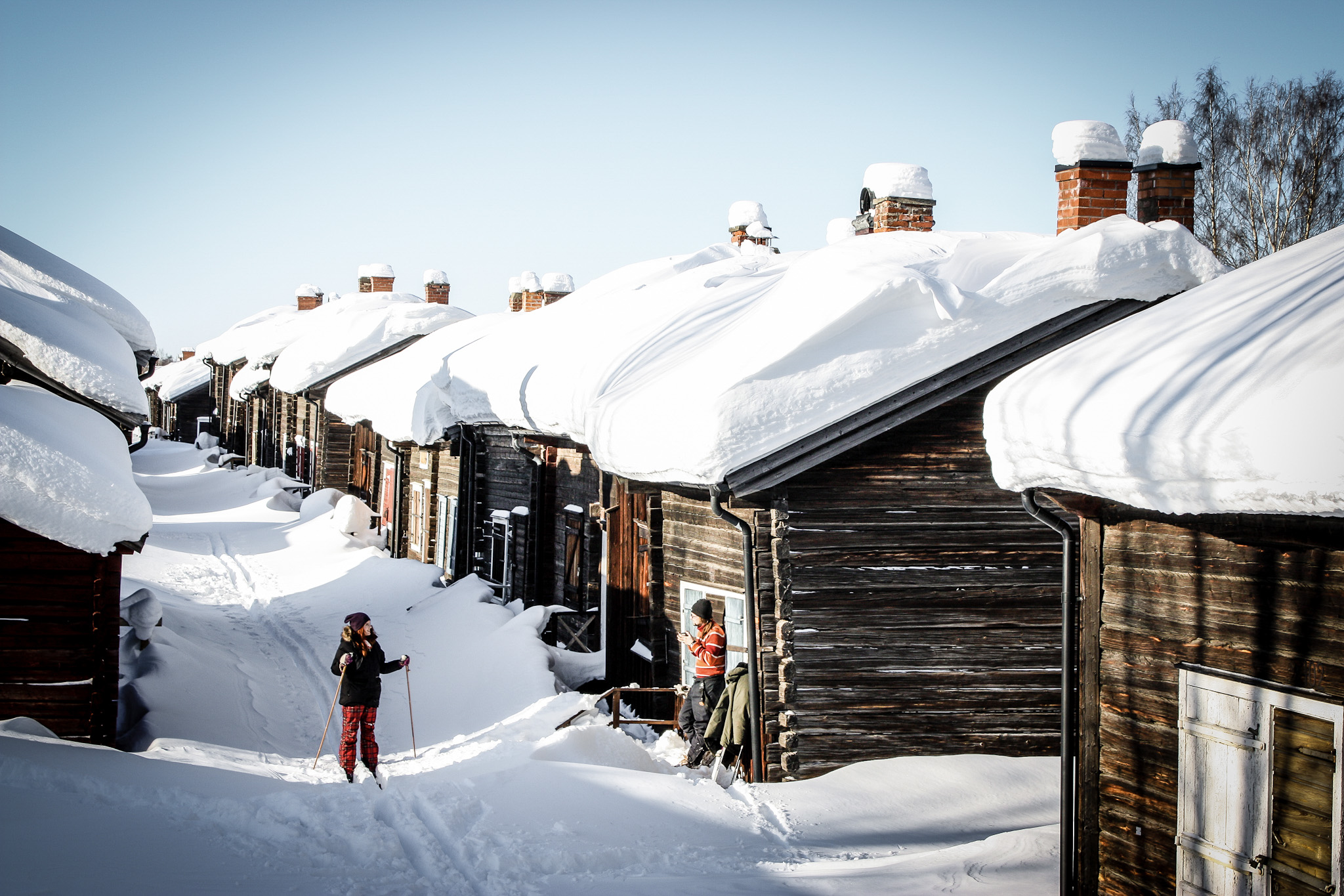 Ett barn åker längdskidor på en snöfylld väg mellan en massa små låga trähus med snö på taket.