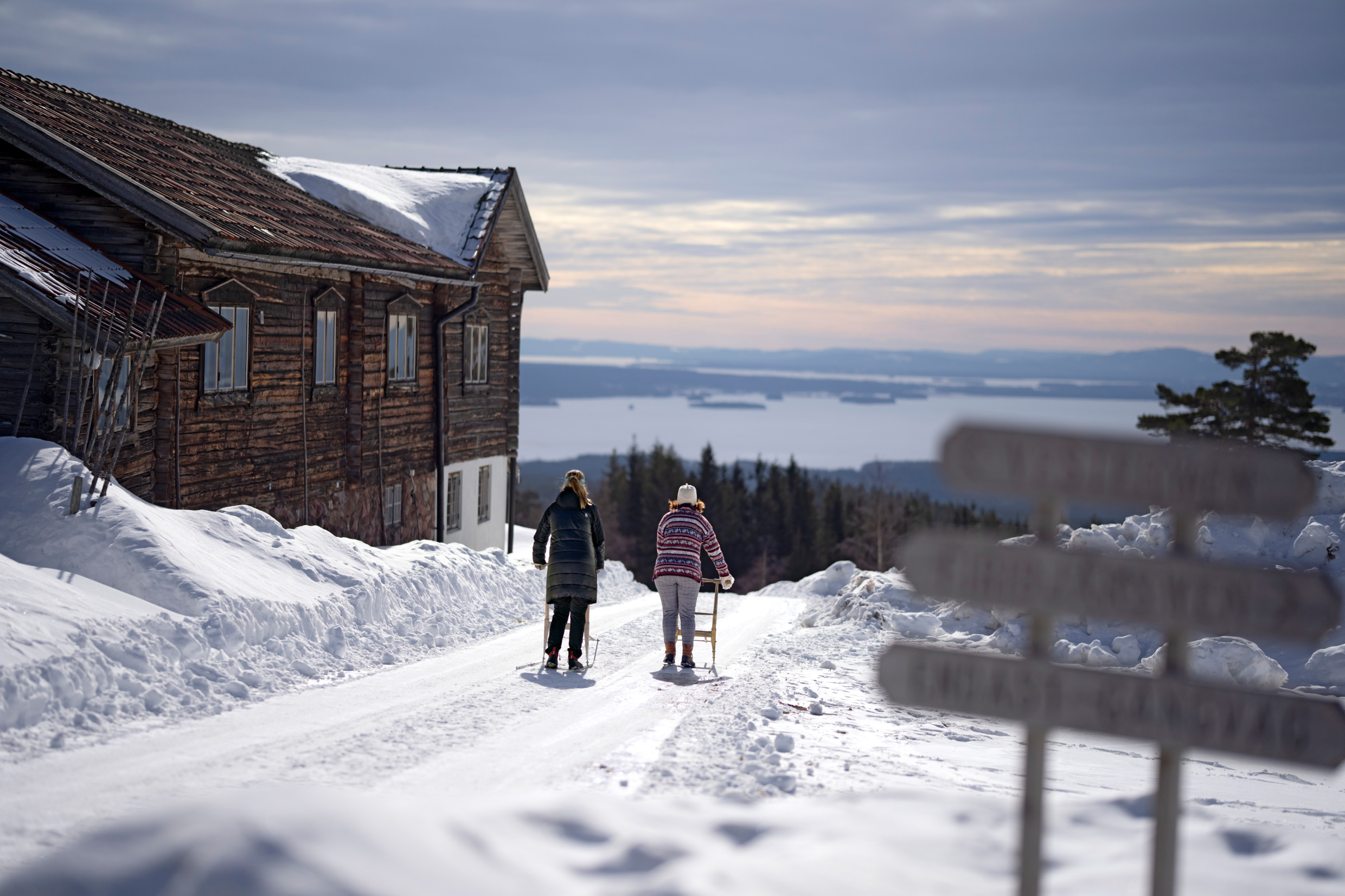Två personer sparkar fram på varsin spark på en soligt snöig vinterväg.