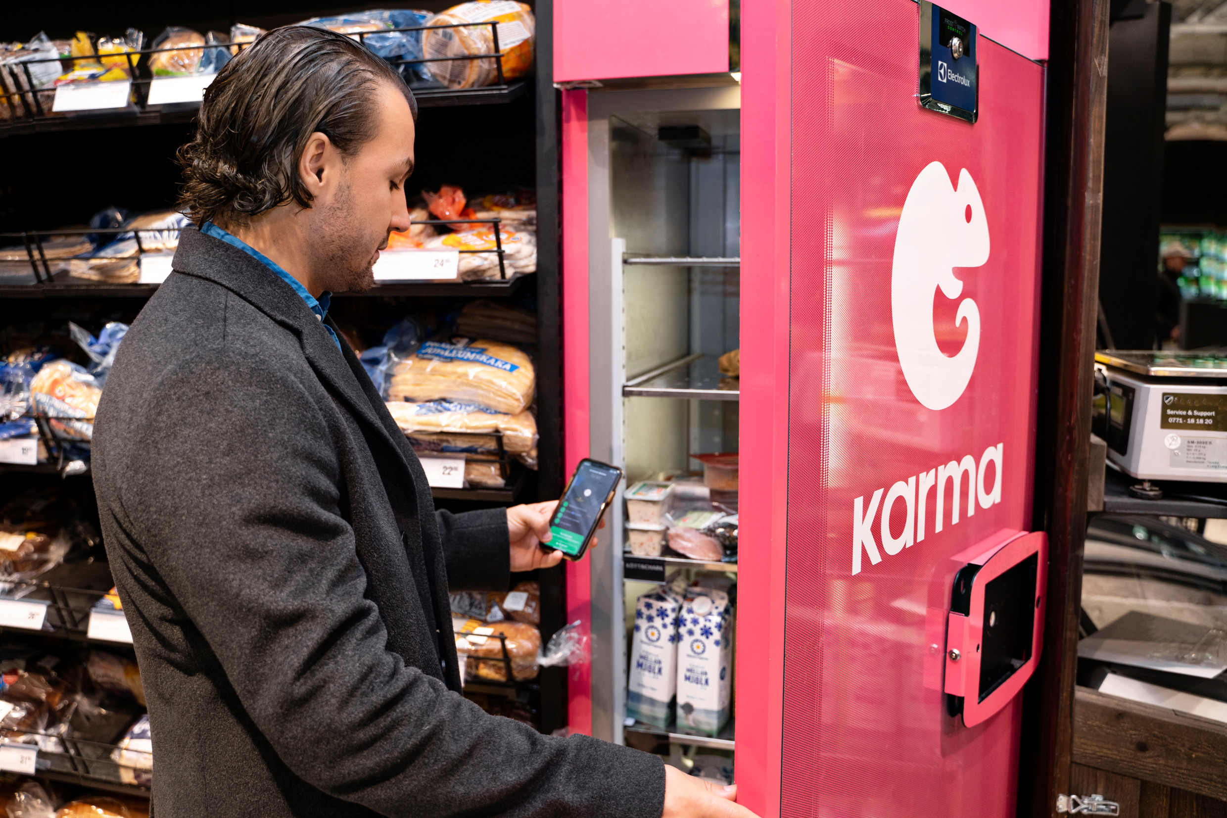 En man står med mobilen i handen framför en liten kyl som det står karma på.