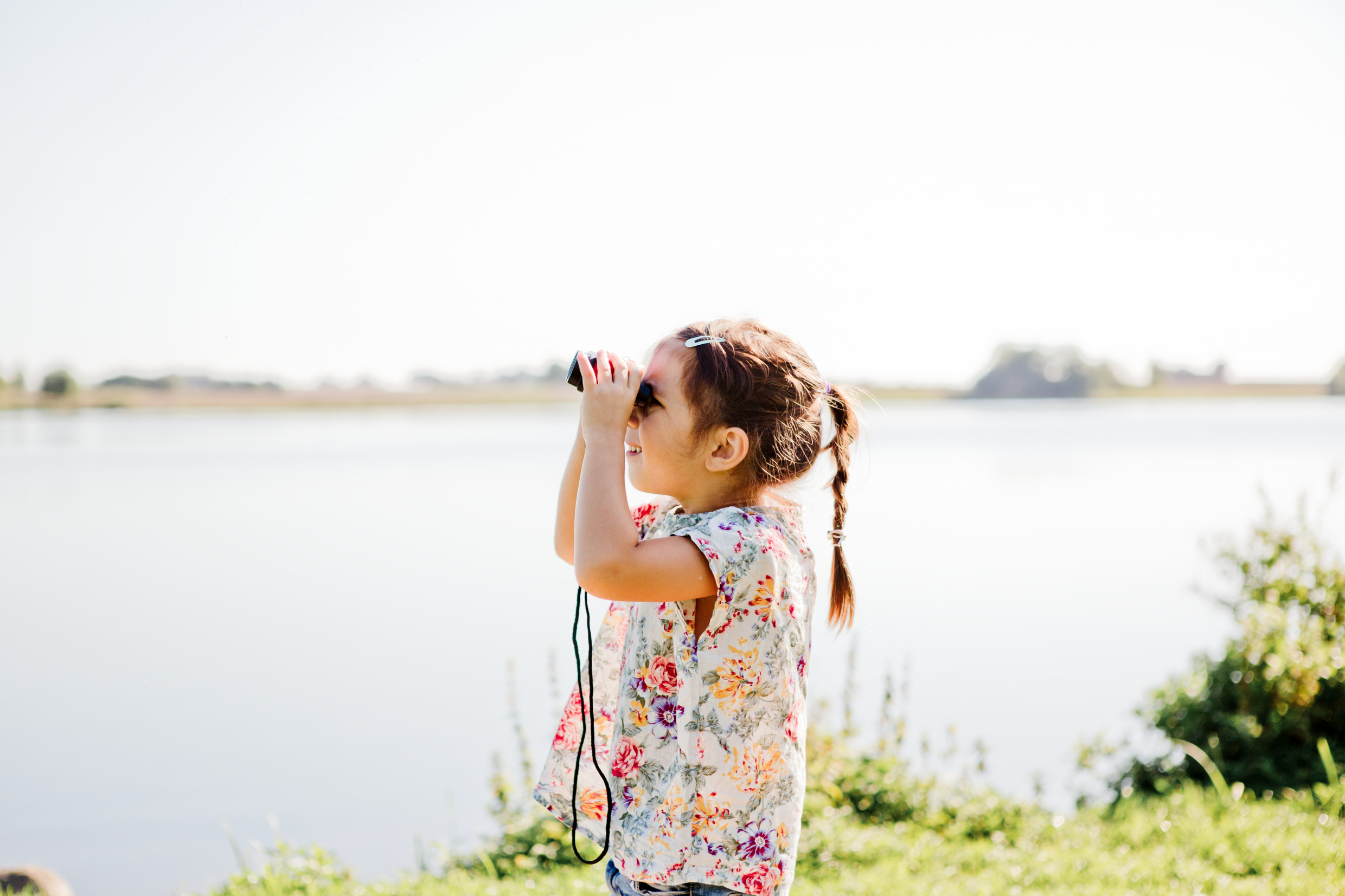 En liten flicka står vid stranden och tittar med en kikare.
