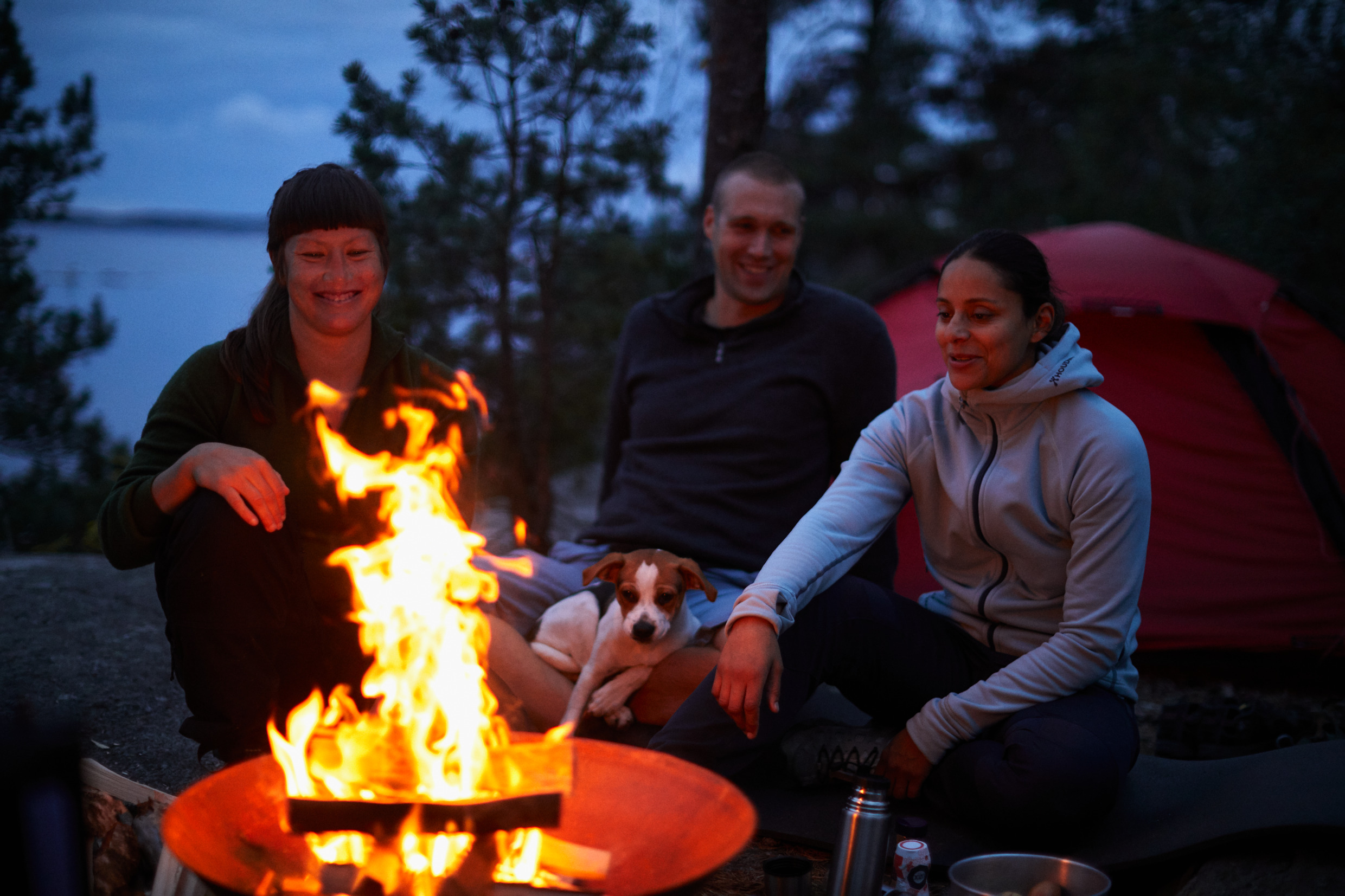 Tre personer lagar mat i skymningen över en öppen eld.