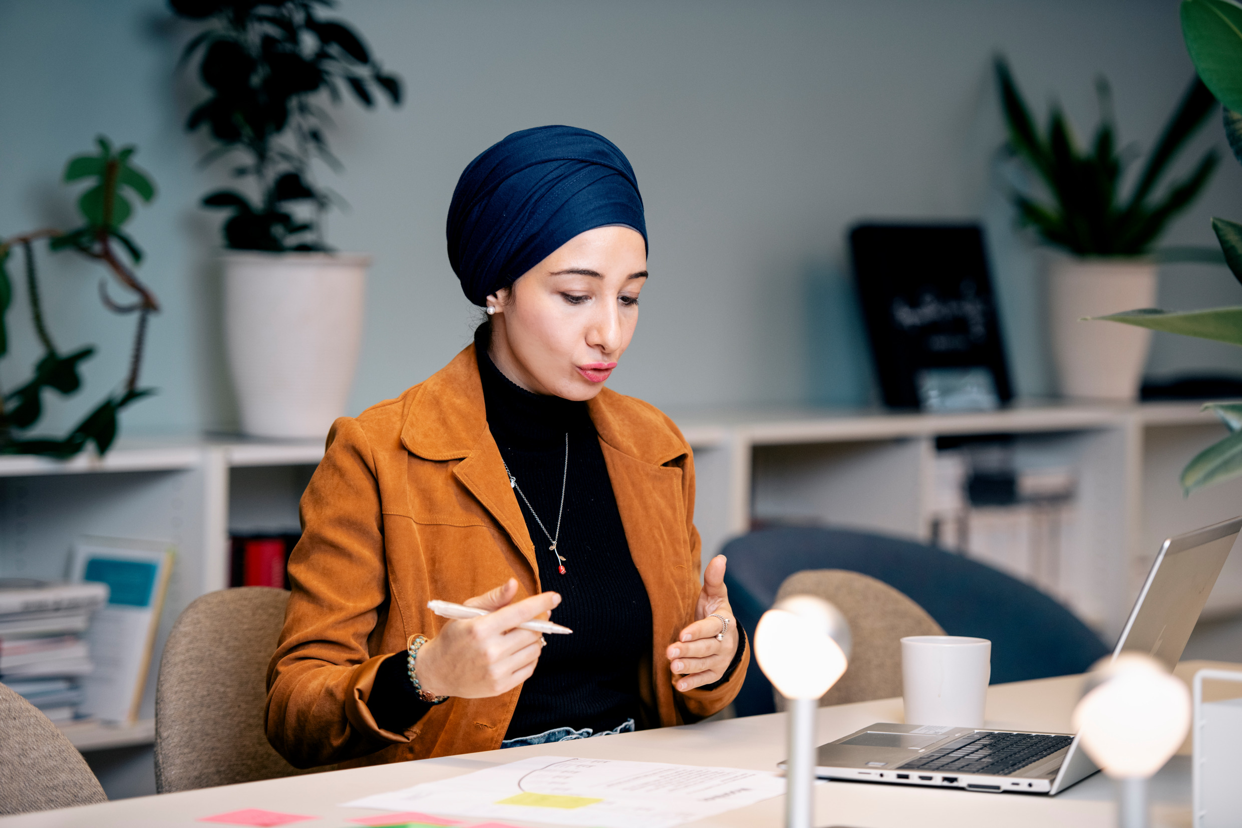 En kvinna sitter vid en bärbar dator i ett konferensbord och pratar i ett digitalt möte.