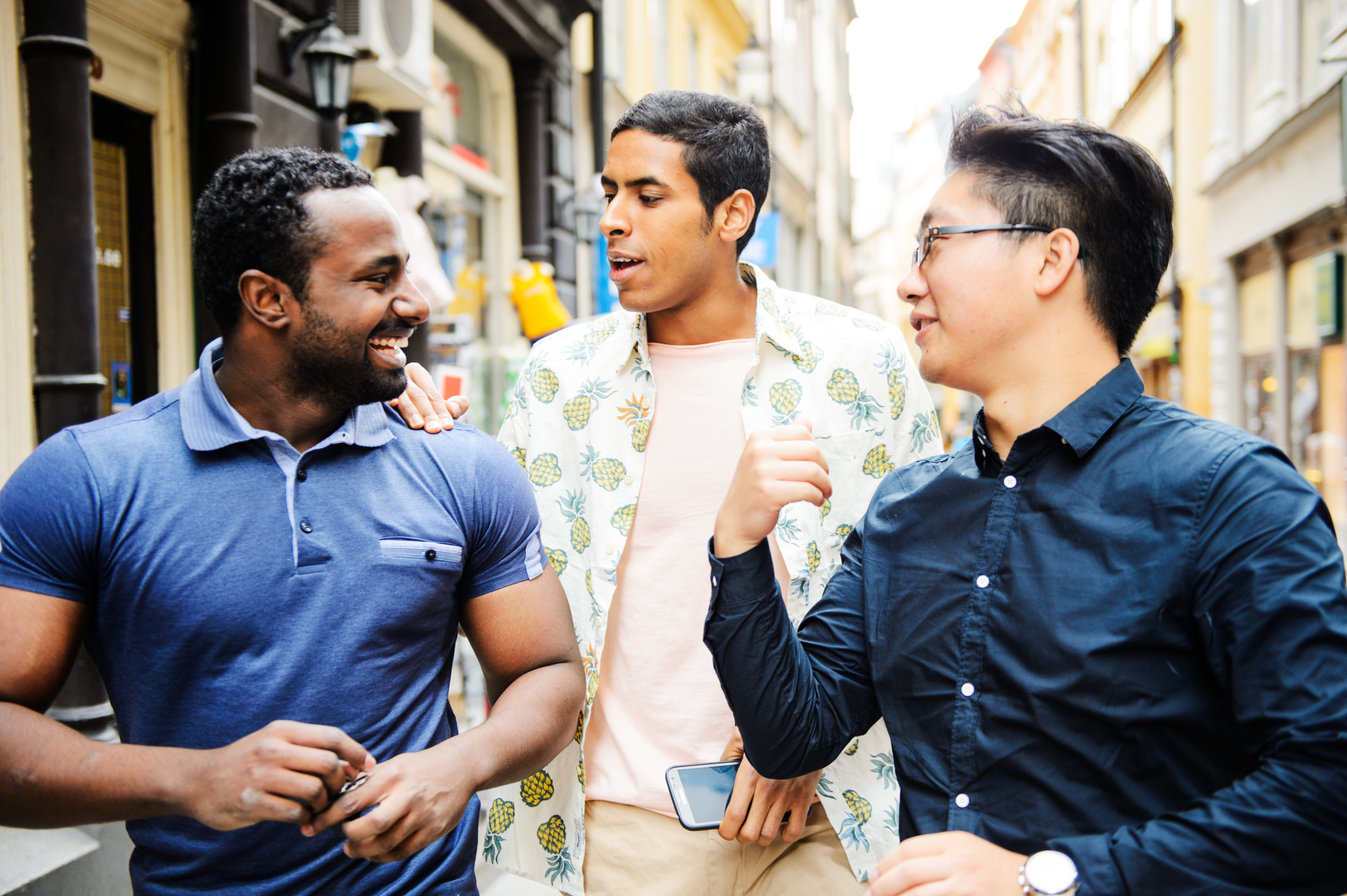 Tre personer tittar på varandra, pratar och ser glada ut. De befinner sig i en stadsmiljö.