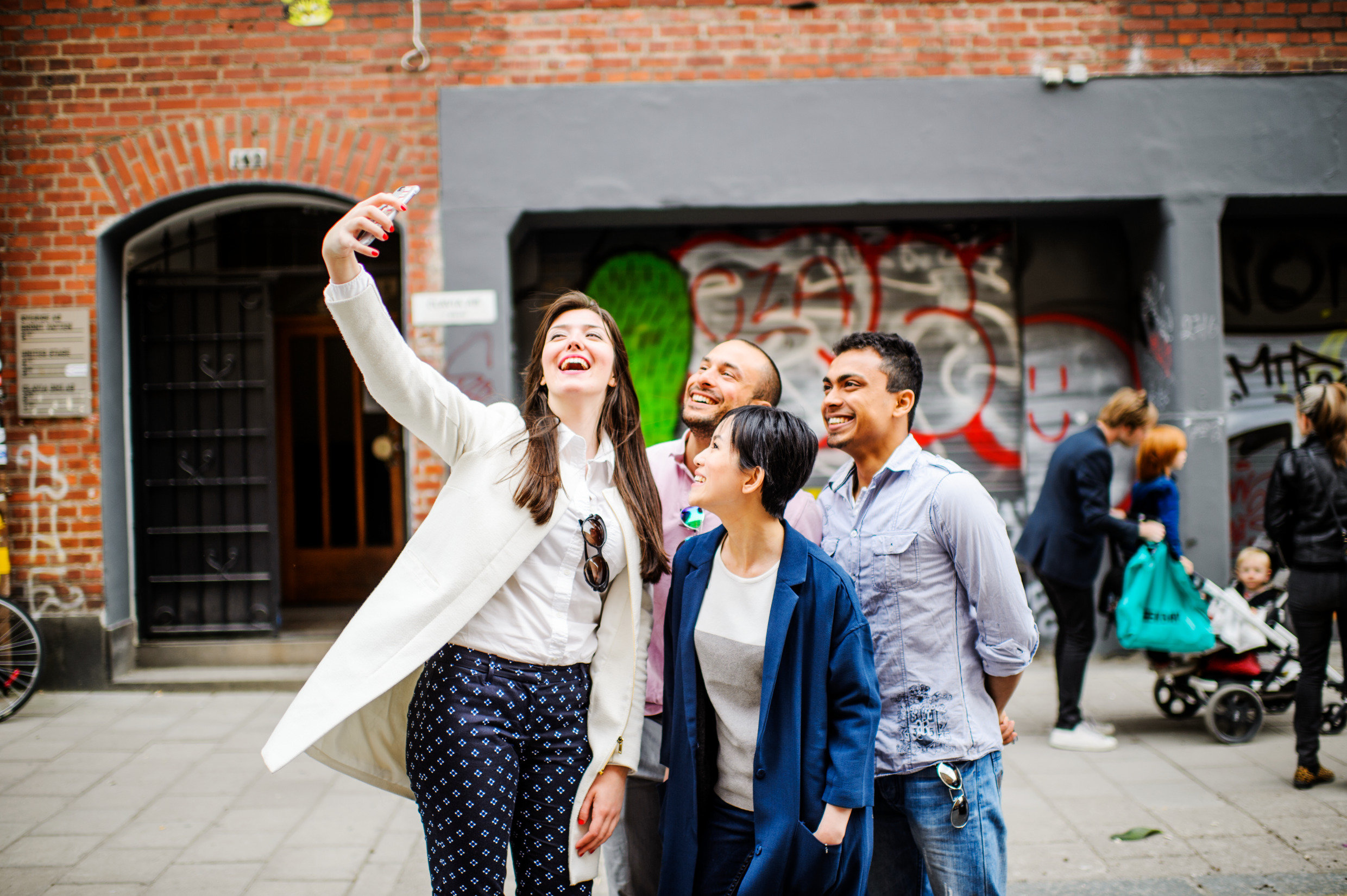 Fyra ungdomar tar ett gruppfoto på varandra utomhus på en bilfri gata i en stad.