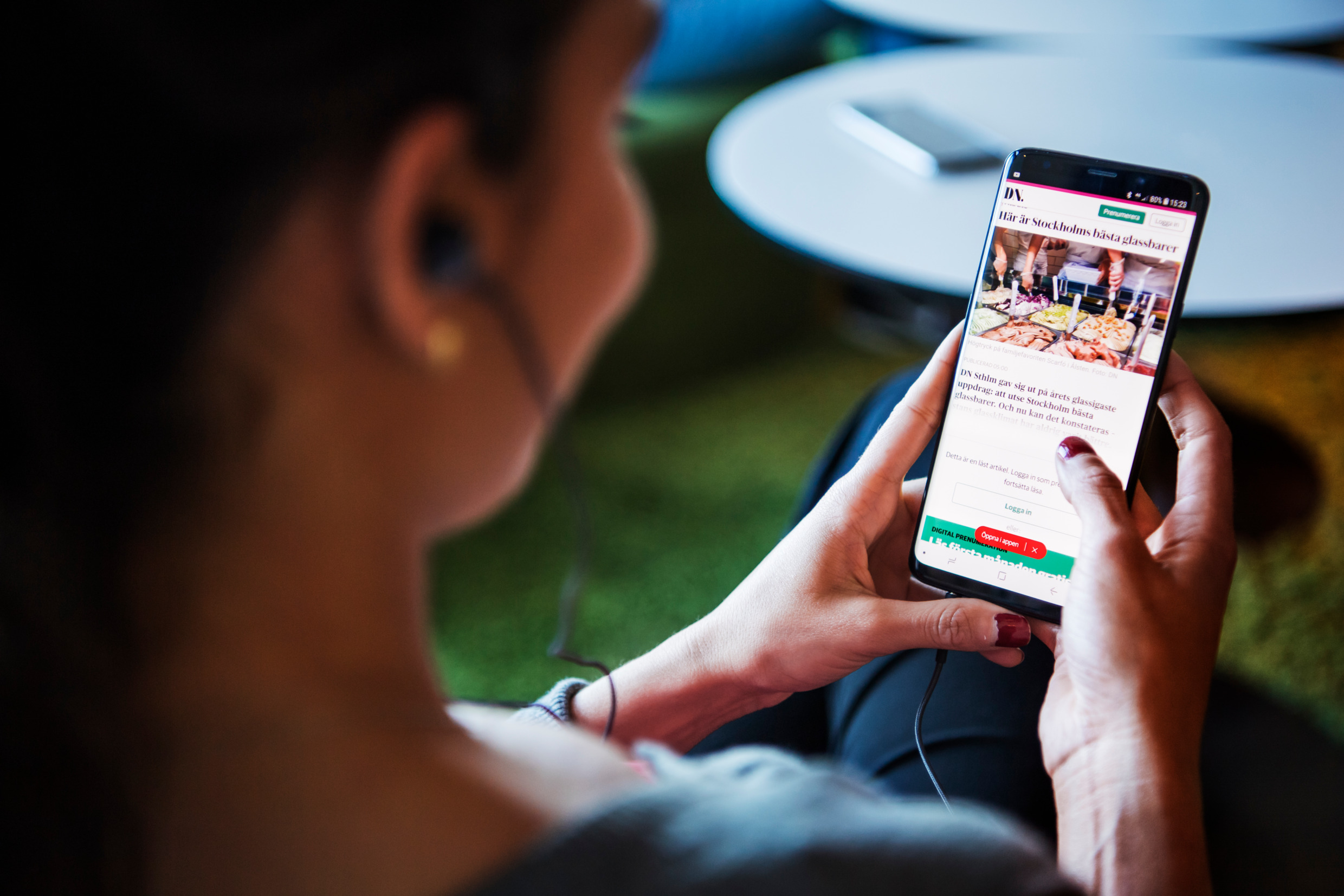 En kvinna sitter med en telefon i knät och surfar på Dagens nyheters webbplats.