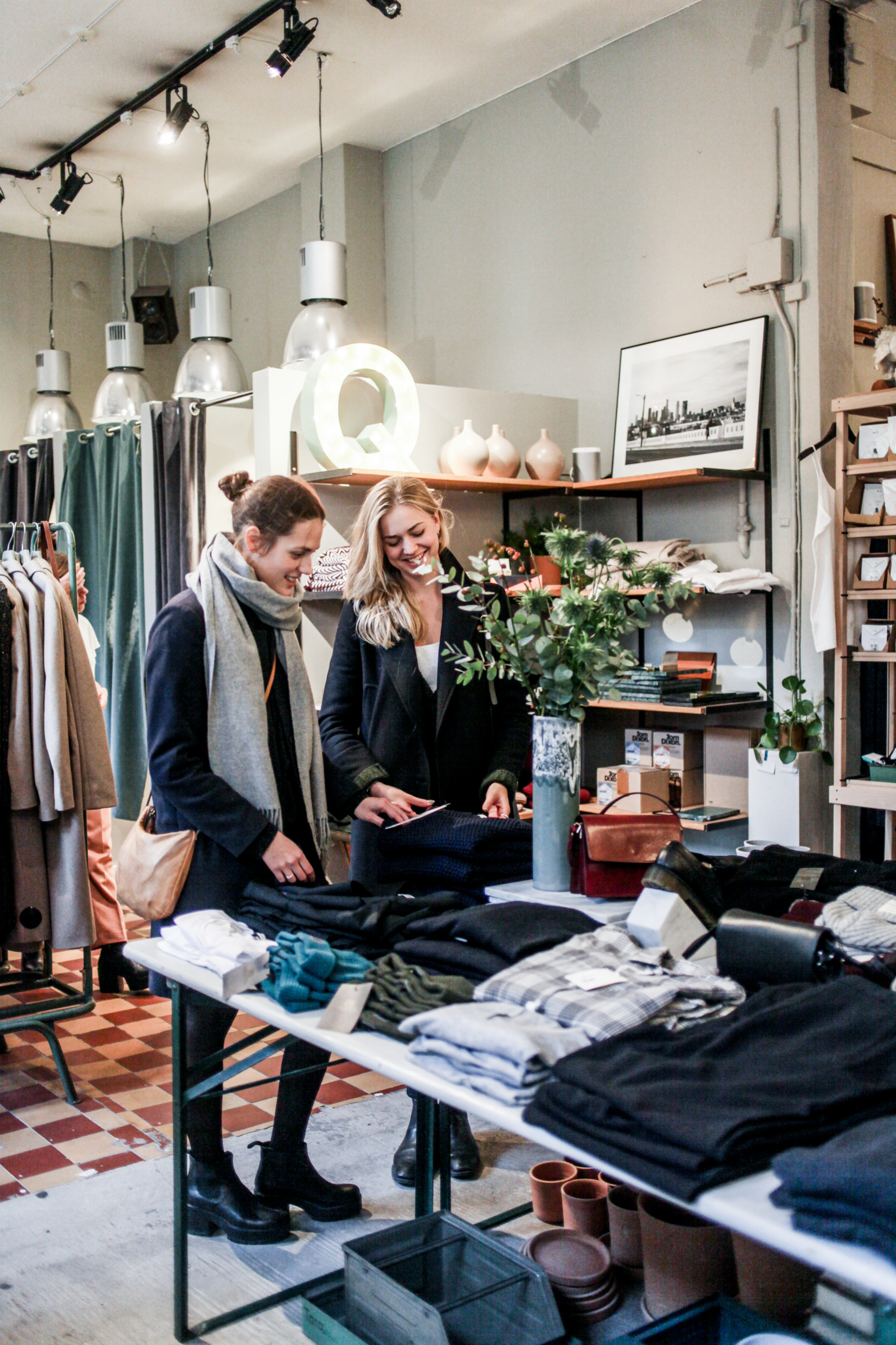 Två tjejer står och pratar och tittar på byxor i en klädesaffär.