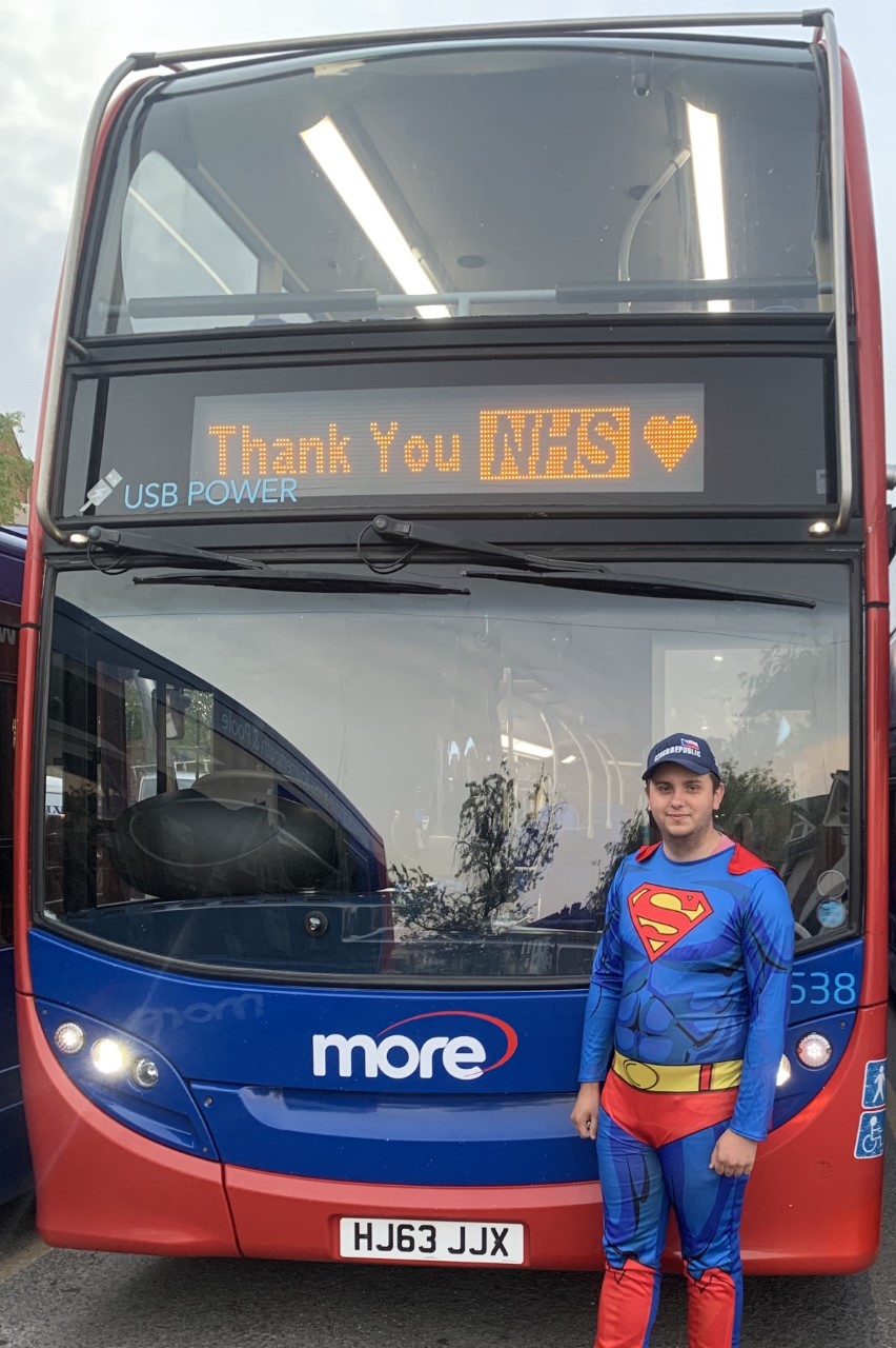 Photo of a morebus bus driver dressed as superman in front of a bus that says 'Thank you NHS'