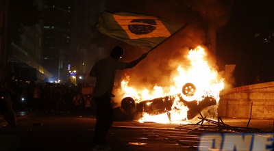 מפגין מנופף בדגל ברזיל על רקע מכונית שרופה (רויטרס)