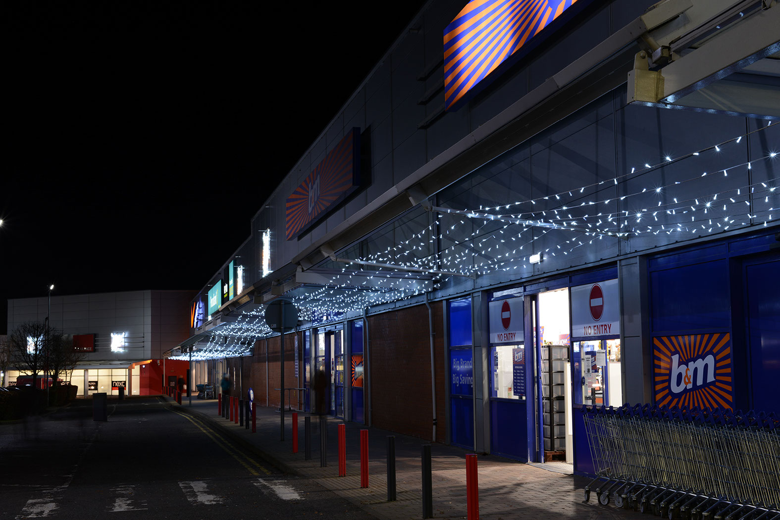 White light ceiling running along the covered walkway outside shops at a retail park