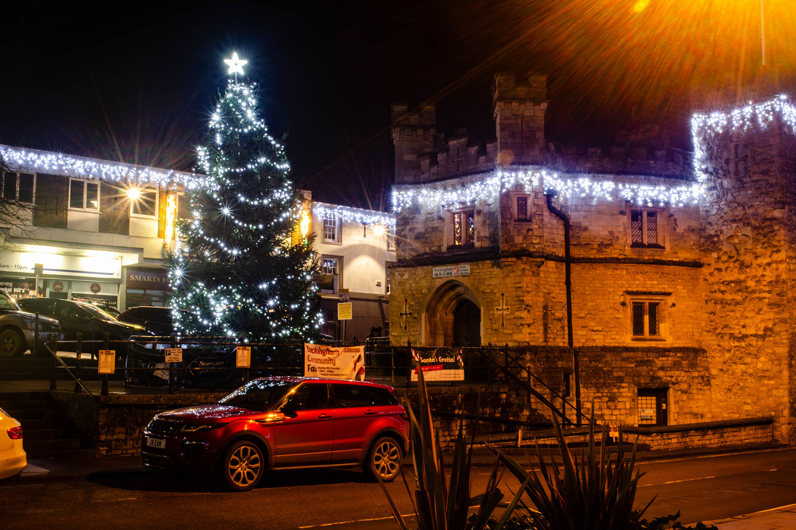 White icicle lights running along the top of a historic gaol with a Christmas tree outside