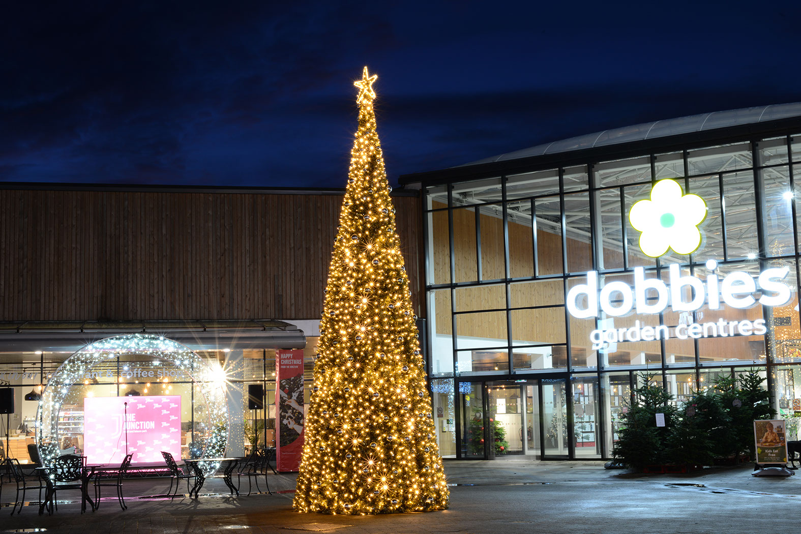 Warm white Christmas cone tree decorated with baubles and a star outside a garden centre