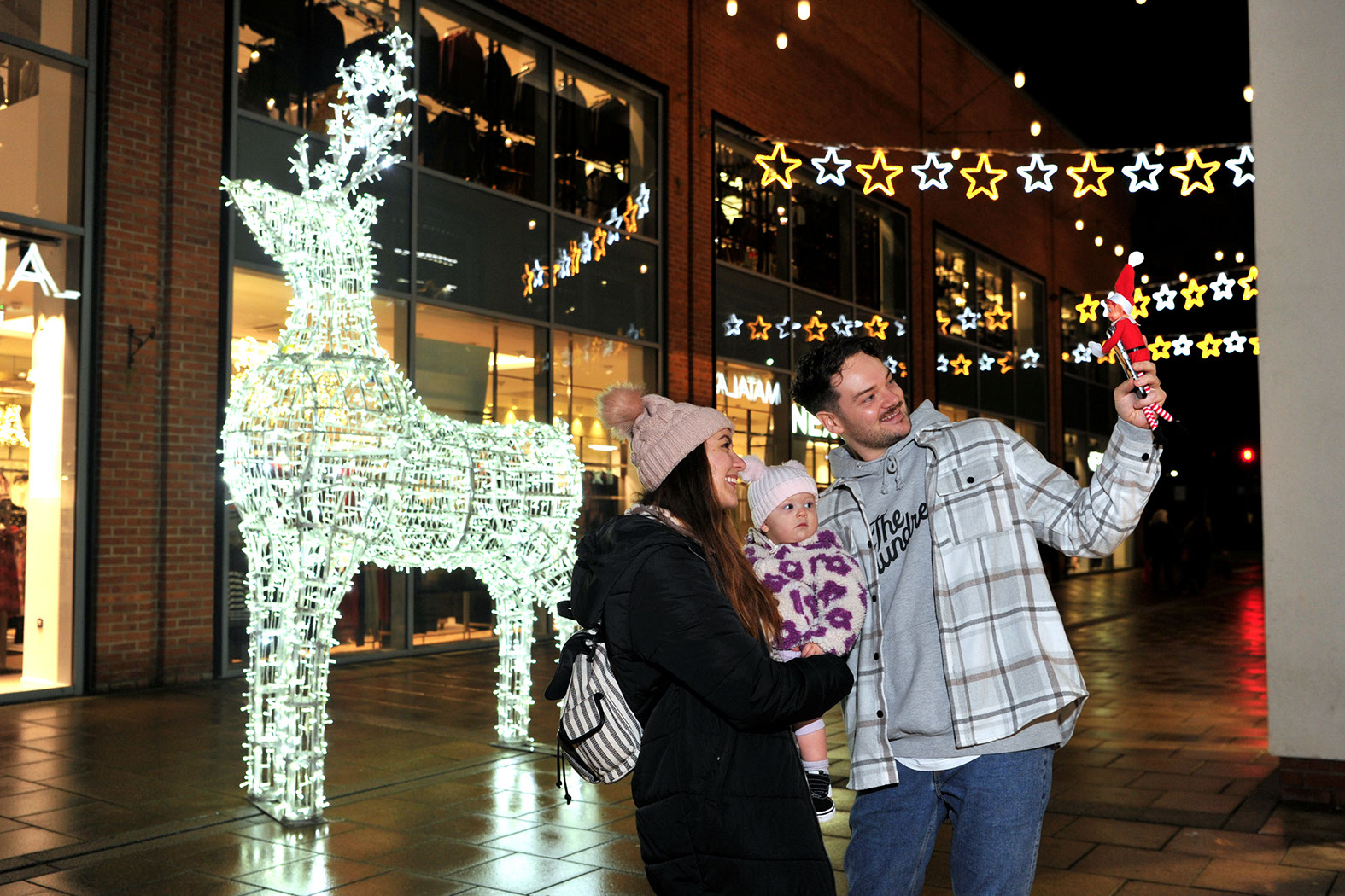 Couple with baby taking a selfie in front of a large illuminated 3D reindeer