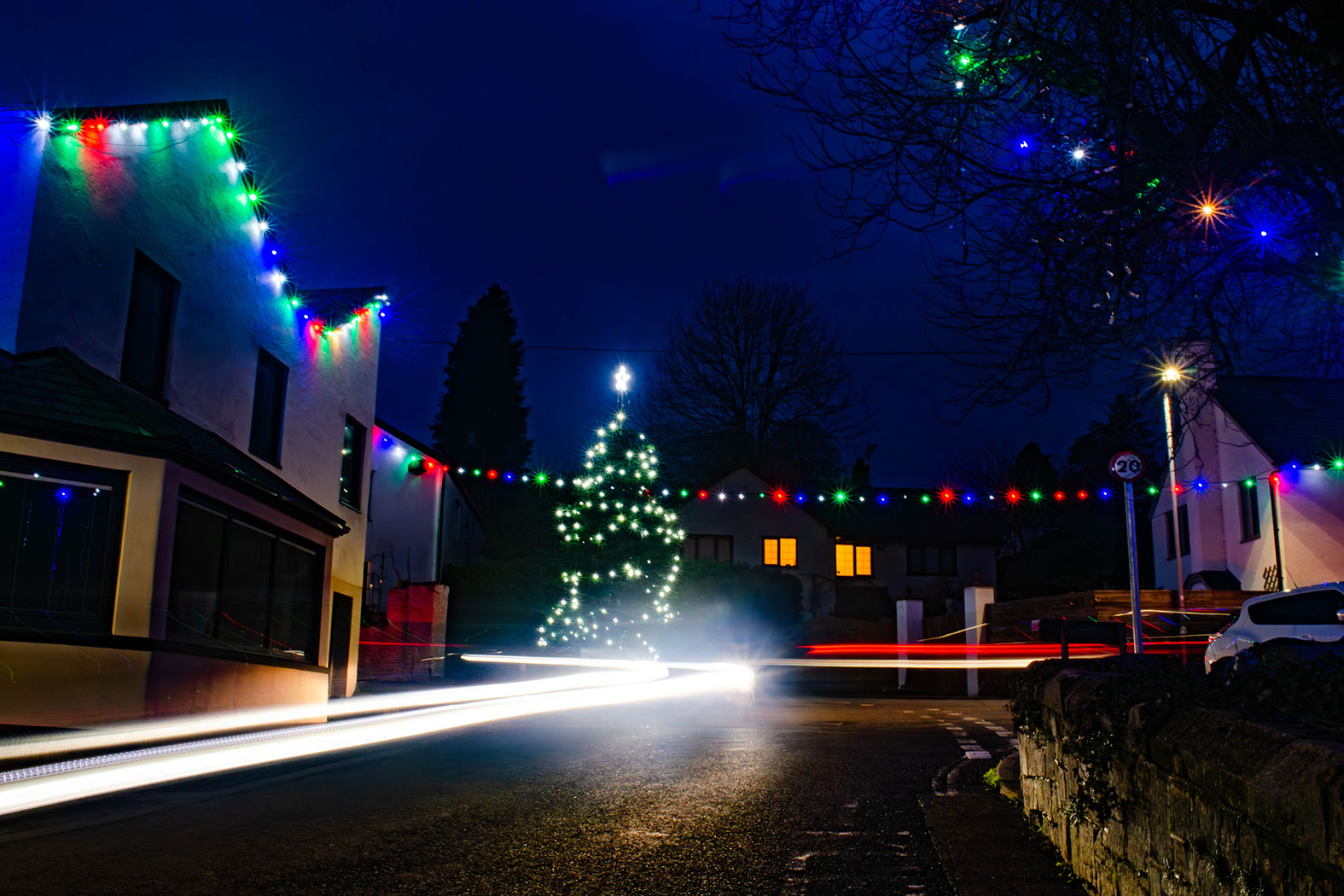 Multicoloured festoon lights running along a street with a Christmas tree in the background