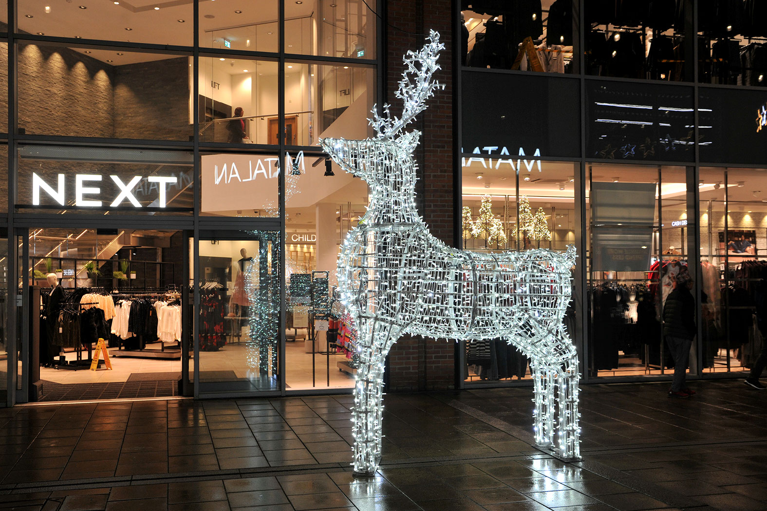 Large white illuminated reindeer positioned in front of a shop