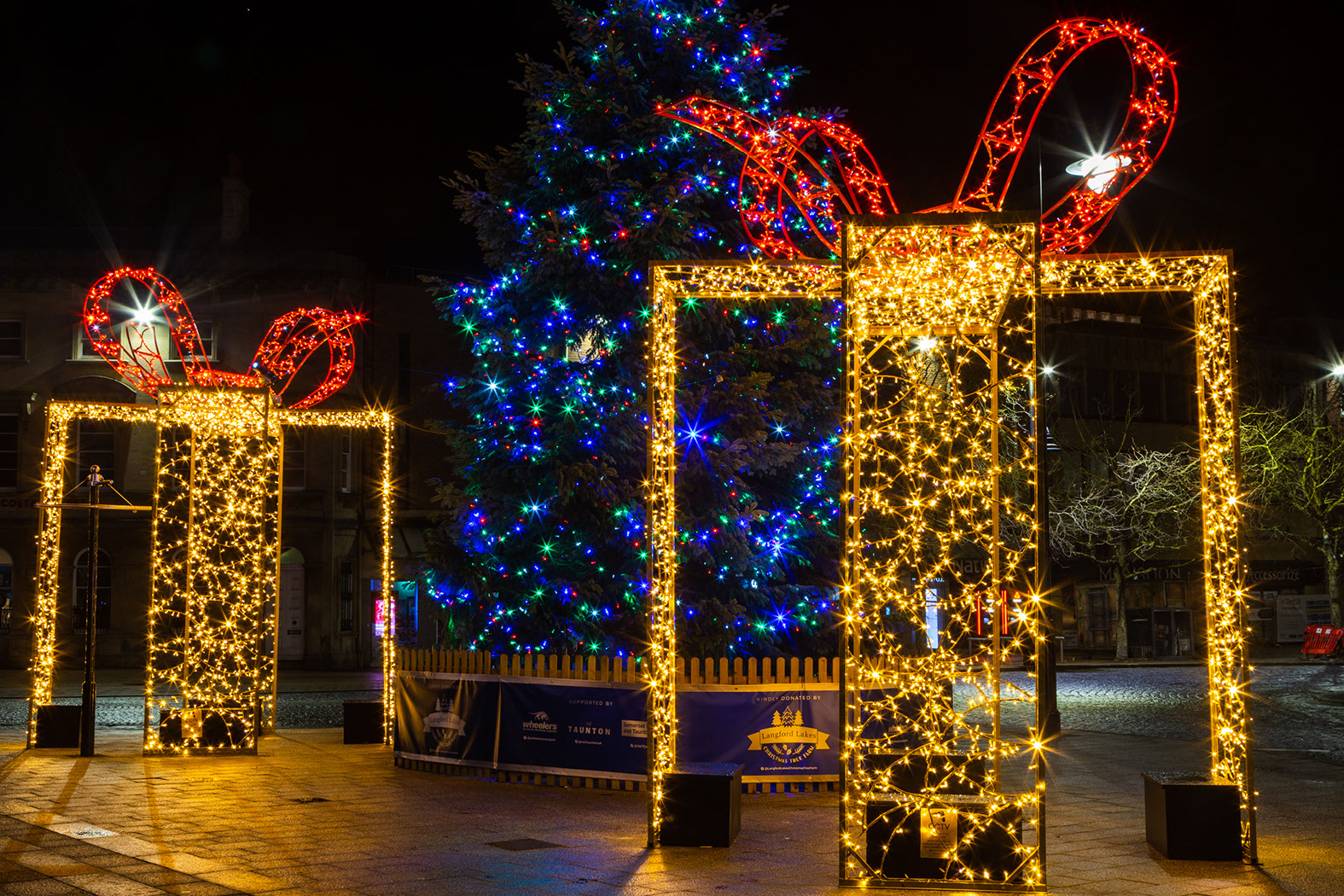 Close-up of large warm white walk-through gift boxes on either side of a Christmas tree
