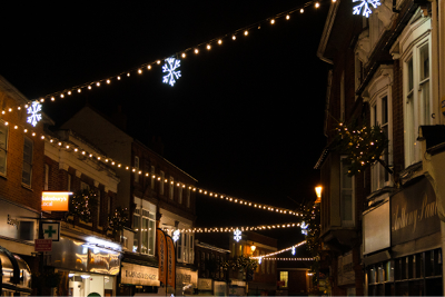 Warm white festoon with white snowflake decorations zig-zagging above a busy Christmas shopping street.