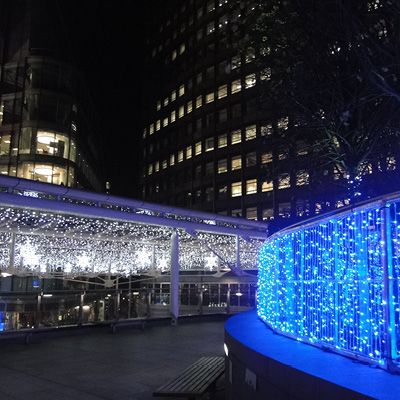 A nighttime outdoor scene features decorative blue light string illuminating a walkway handrail with icicles and snowflake lit motifs in the background creating a festive atmosphere.