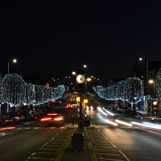 A city street at night with a row of trees decorated with lights.