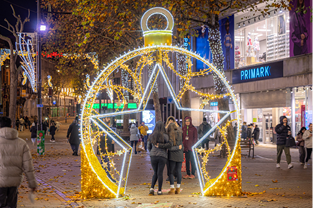 Couple of girls having their photo taken under a Star Bauble Arch in busy shopping street