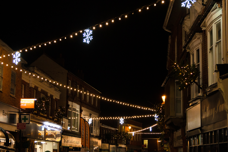 Warm white festoon with white snowflake decorations zig-zagging above a busy Christmas shopping street.