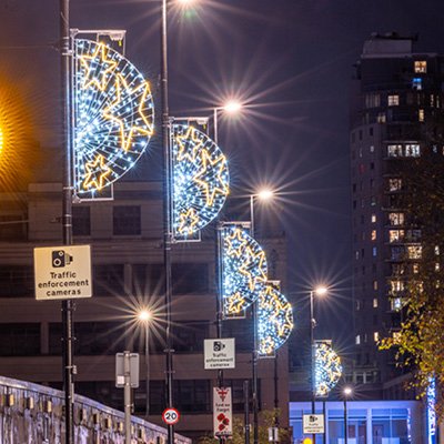 A row of streetlights illuminate a dark night sky with decorative semi-circular discs with stars as column motifs visible on the left side.