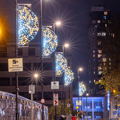A row of streetlights illuminate a dark night sky with decorative semi-circular discs with stars as column motifs visible on the left side.