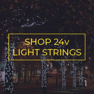 Commercial light strings wrapped around low-level tree trunks along a town centre road