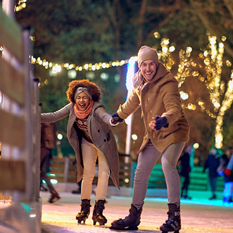Couple ice skating under trees lit up with light strings.