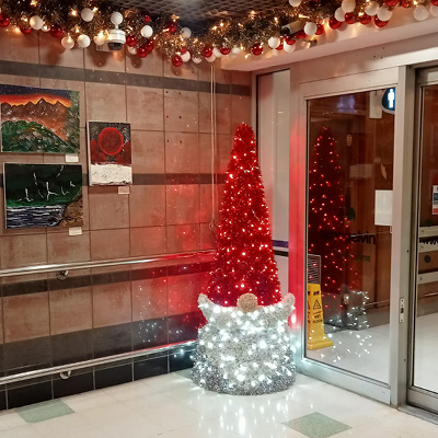 An indoor shopping centre entry way decorated with  gold garland with red and gold baubles attached to the ceiling and an illuminated gonk styled as santa.