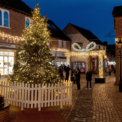 People walking near a building decorated with bright warm white icicle lights and a Christmas tree.