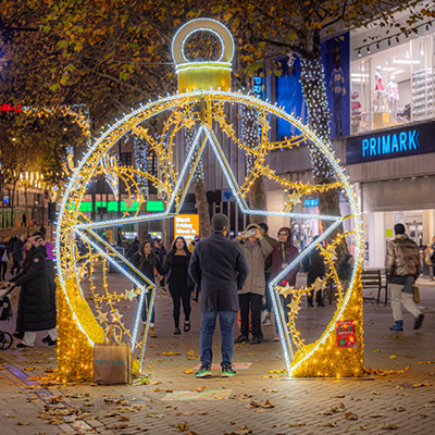 People standing around and taking photos around a large illuminated bauble arch decoration on a city street at night.