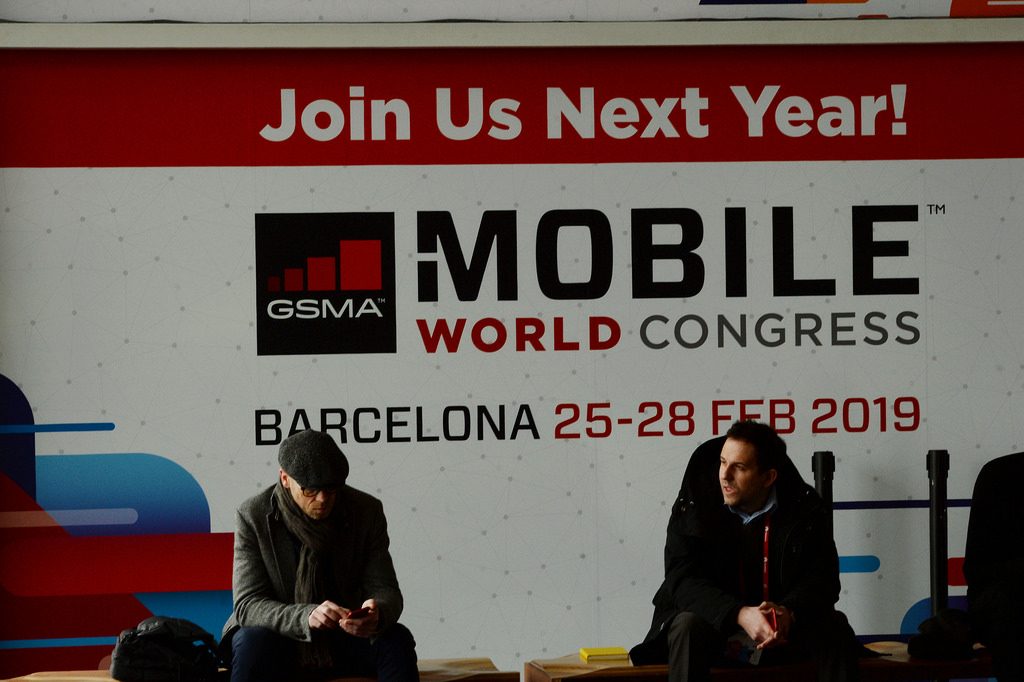 Dos personas están sentadas con un cartel detrás de la Mobile World Congress