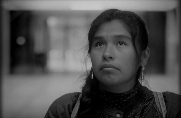 still from Song Without A Name, 2019. This black and white image of a young woman’s face and shoulders shows Geo off-centre. Her eyes are looking up, her mouth is turned down, hair tied back but loose around her face