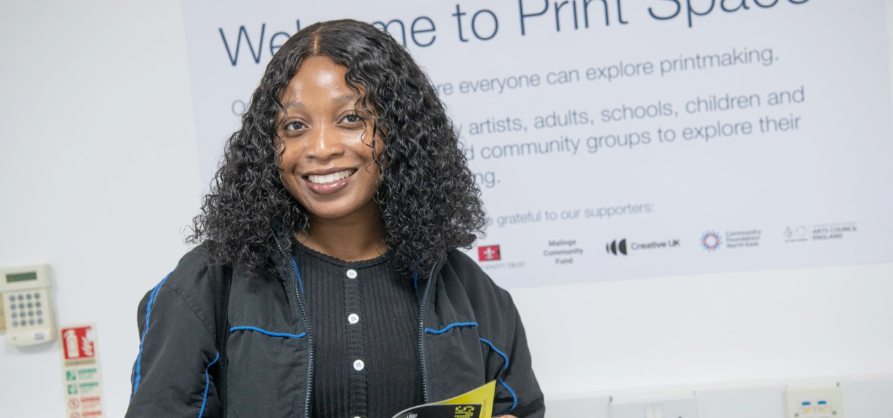 Girl smiling while looking at the brochure - in front of a white wall mural reads `Print Space`