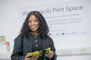Girl smiling while looking at the brochure - in front of a white wall mural reads `Print Space`